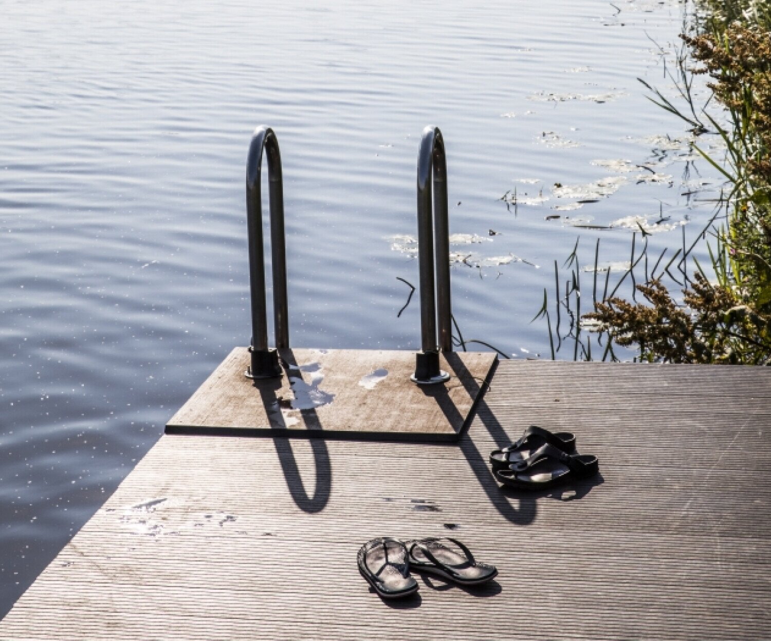 Slippers op de zwemsteiger van zwemmers die in de rivier aan het zwemmen zijn.
